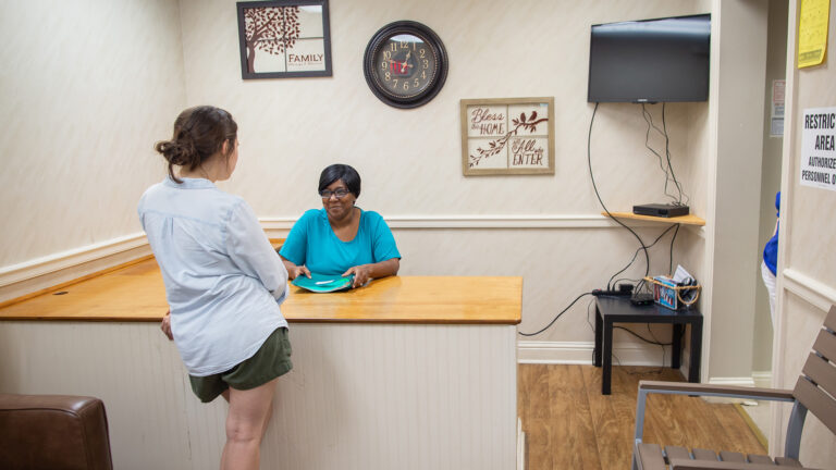 A patient stands at the reception desk speaking with a Murphy-Harpst employee in a clinic's waiting area, adorned with wall decor that provides a homey atmosphere.